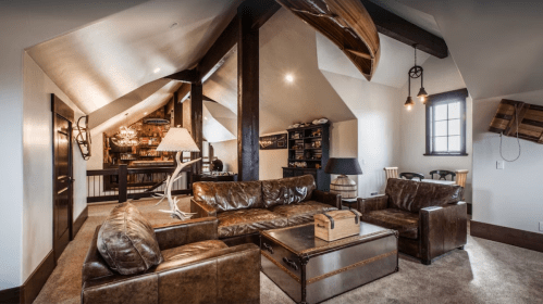 Cozy attic living room with leather sofas, wooden beams, and a warm ambiance, featuring a bookshelf and dining area.